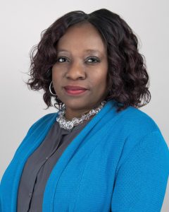 This is an image of Nadine Cherenfant-Colas, licensed mental health counselor from NewVision Healthcare Group. She is a Black woman with shoulder length wavy, dark brown hair. She is wearing a turquoise jacket over a grey blouse and a silver necklace.